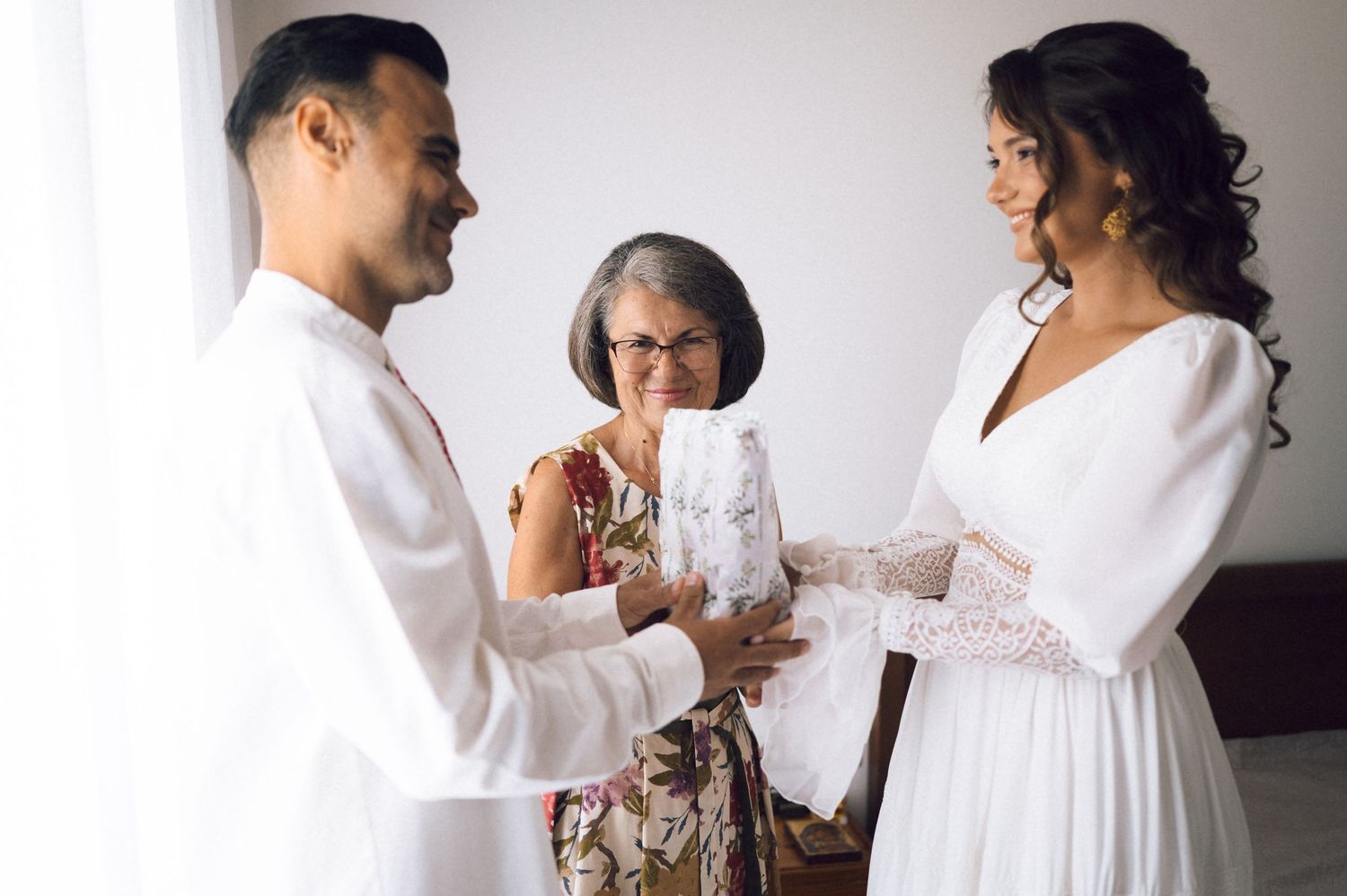 Bride and groom exchanging vows with an older woman officiating during an intimate indoor wedding ceremony.