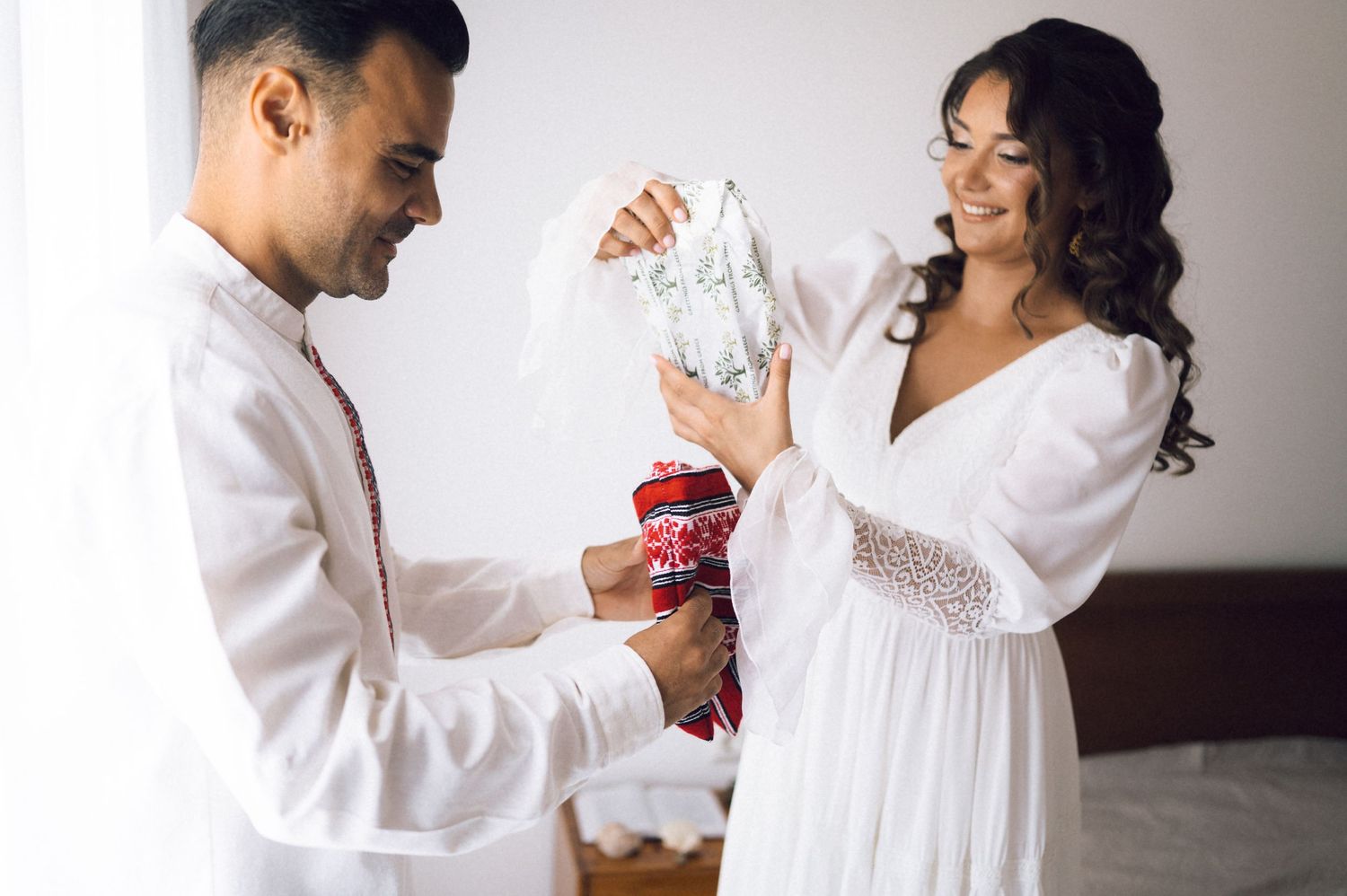 Bride and groom in white outfits exchanging wedding gifts with smiles on their special day.