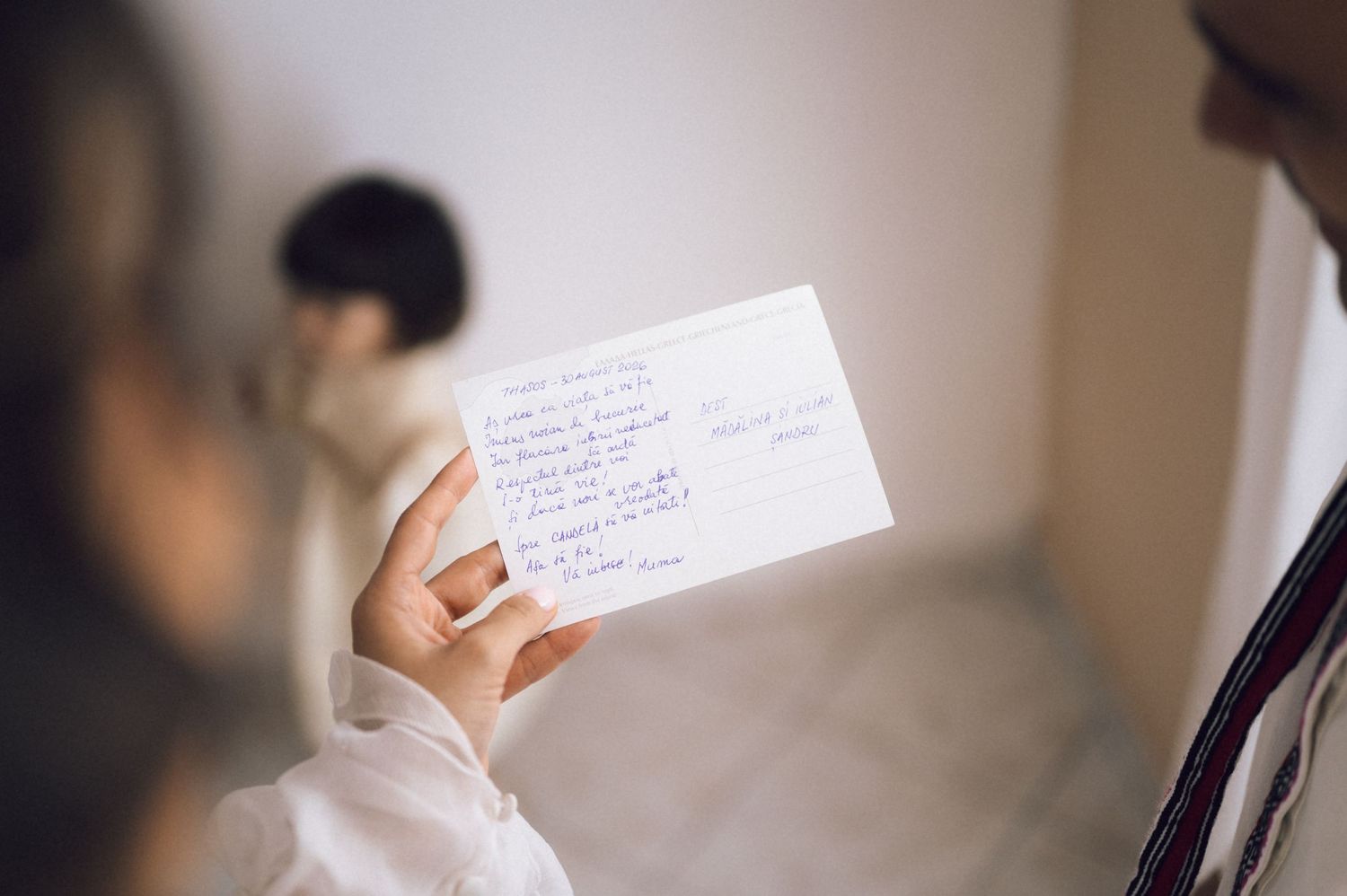 Person holding a handwritten note card indoors with blurred figures in the background.