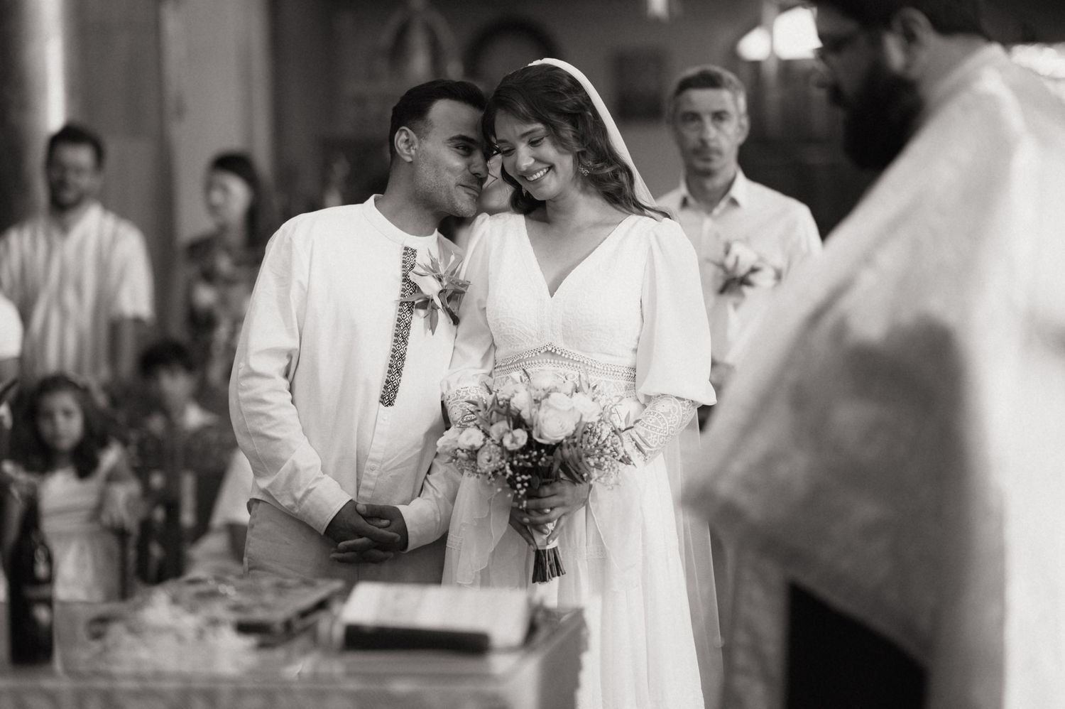 Black and white wedding photo of smiling bride and groom during ceremony, bride holding bouquet.