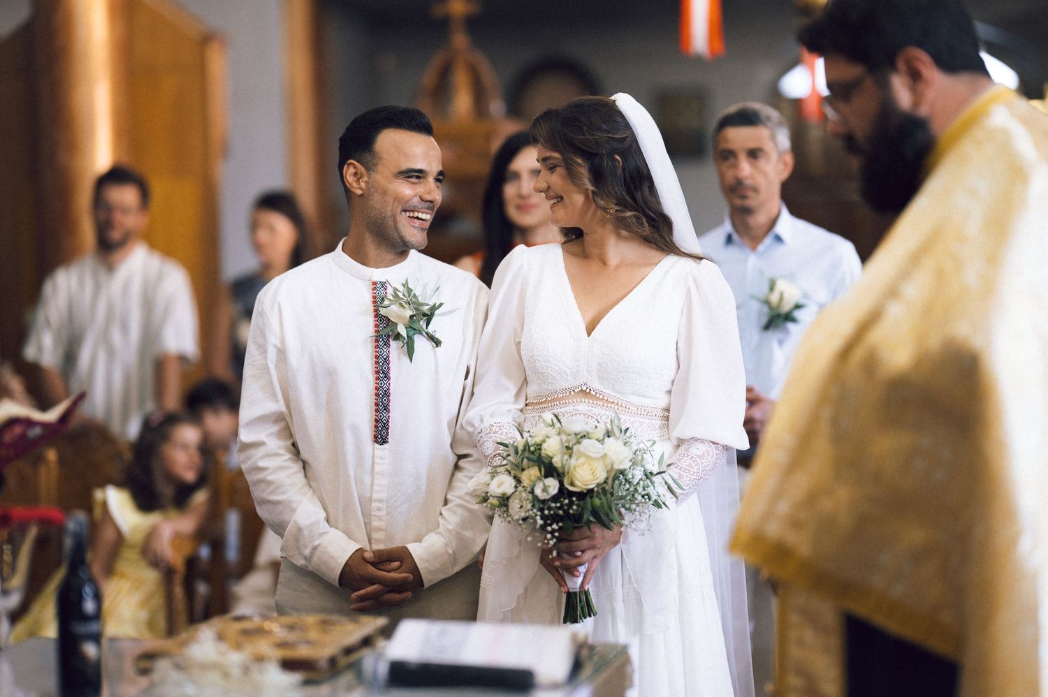 Bride and groom smiling during a traditional church wedding ceremony, bride holding a white floral bouquet.