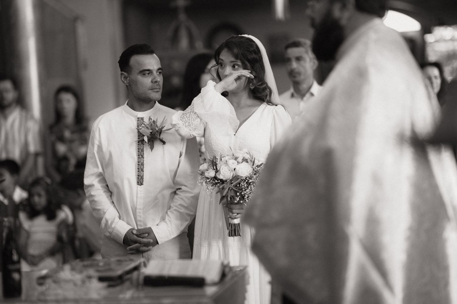 Black and white wedding ceremony photo of bride and groom standing at altar with officiant in elegant church setting.