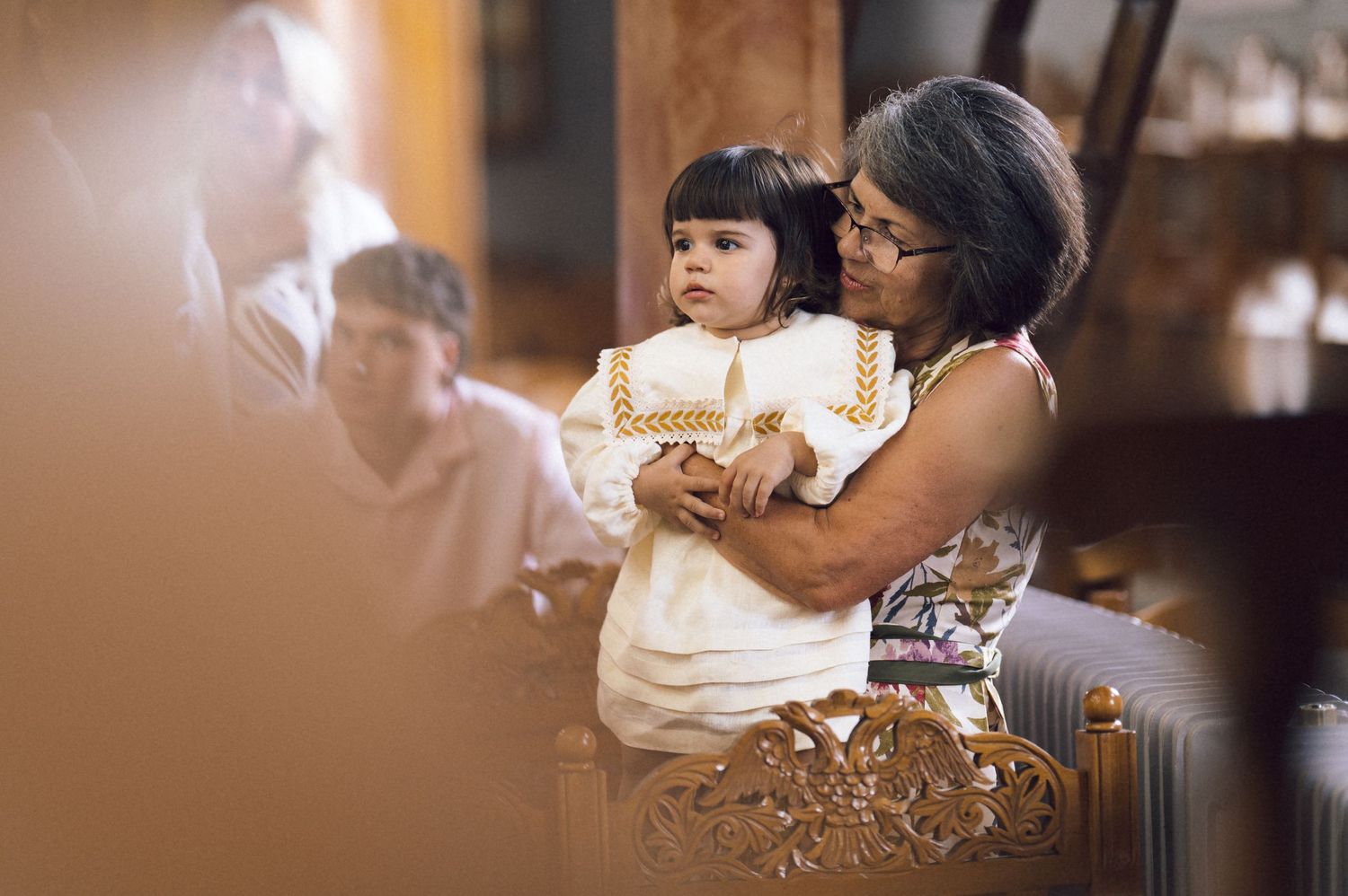 Grandmother holding a baby in white christening gown during a church baptism ceremony.