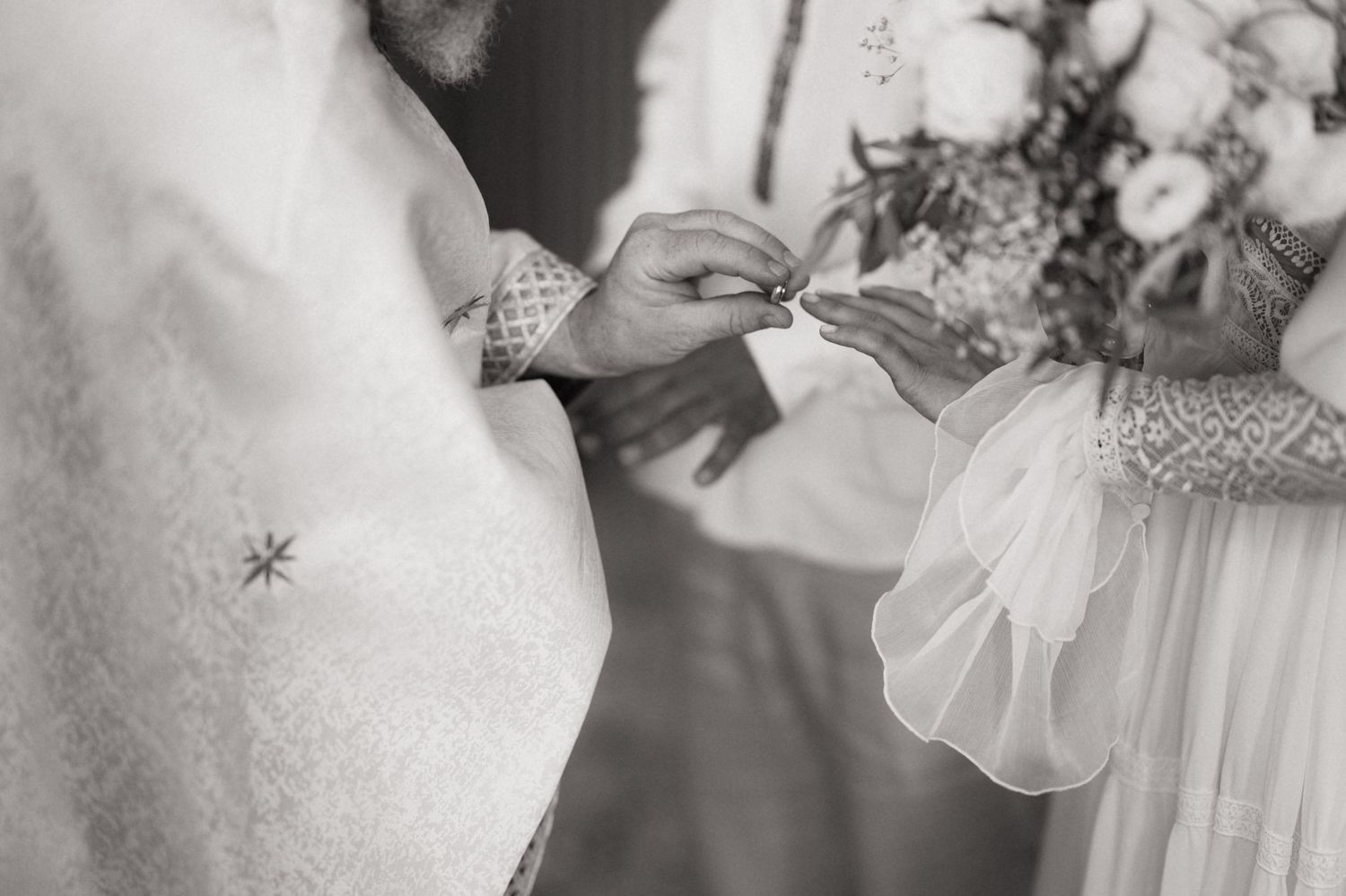 Black and white wedding ring exchange ceremony photo with bouquet and lace dress details.