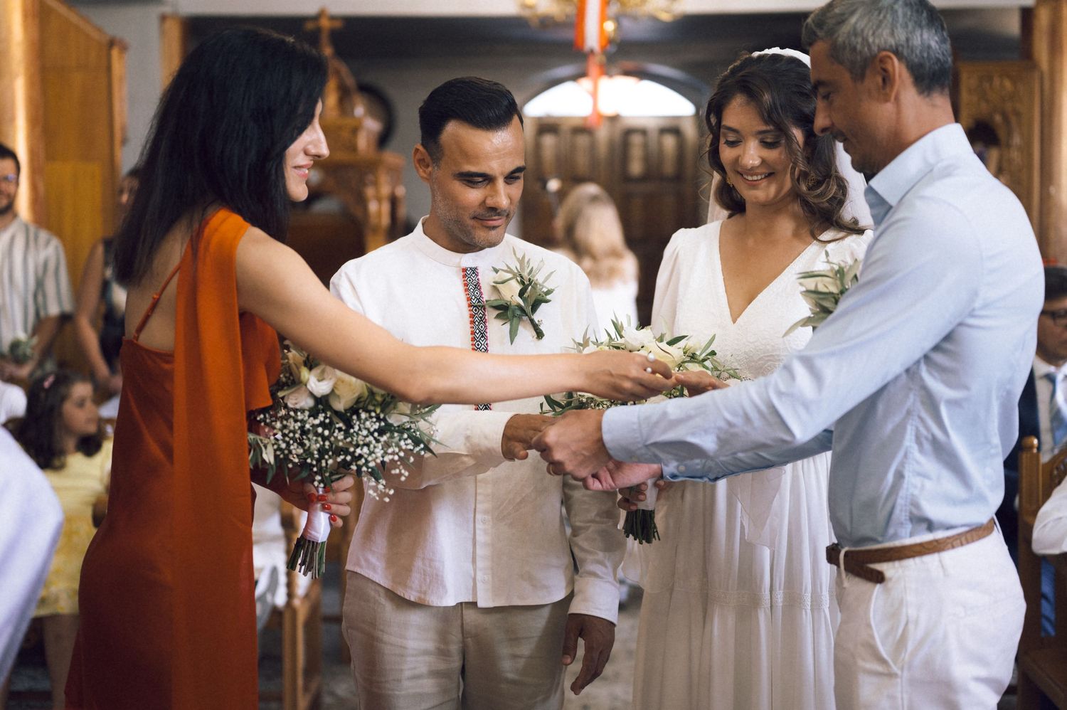 Wedding ceremony with bride in white dress, groom, and guests exchanging flowers in a decorated church.
