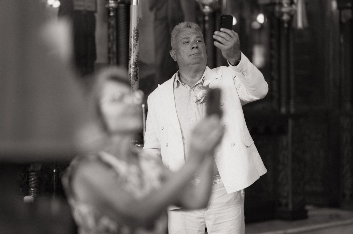Black and white photo of a man in white suit holding a candle during a religious ceremony.