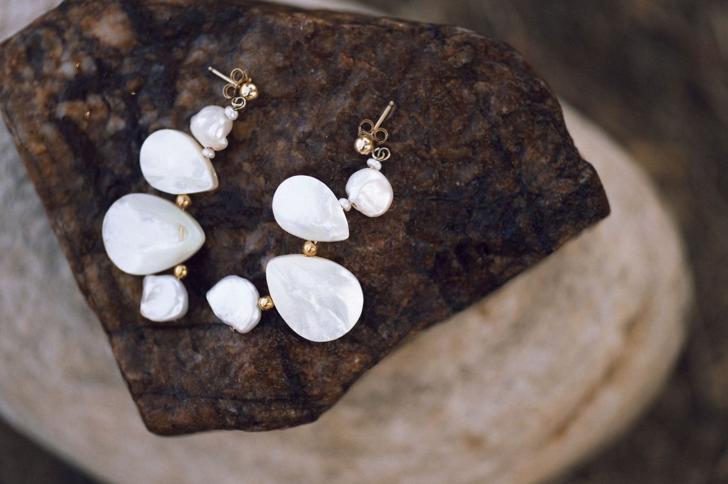 Elegant white freshwater pearl drop earrings with gold accents displayed on a rustic stone surface.