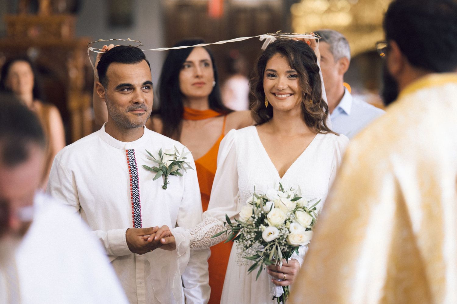 Smiling bride holding white bouquet and groom in white shirt stand together during a church wedding ceremony.