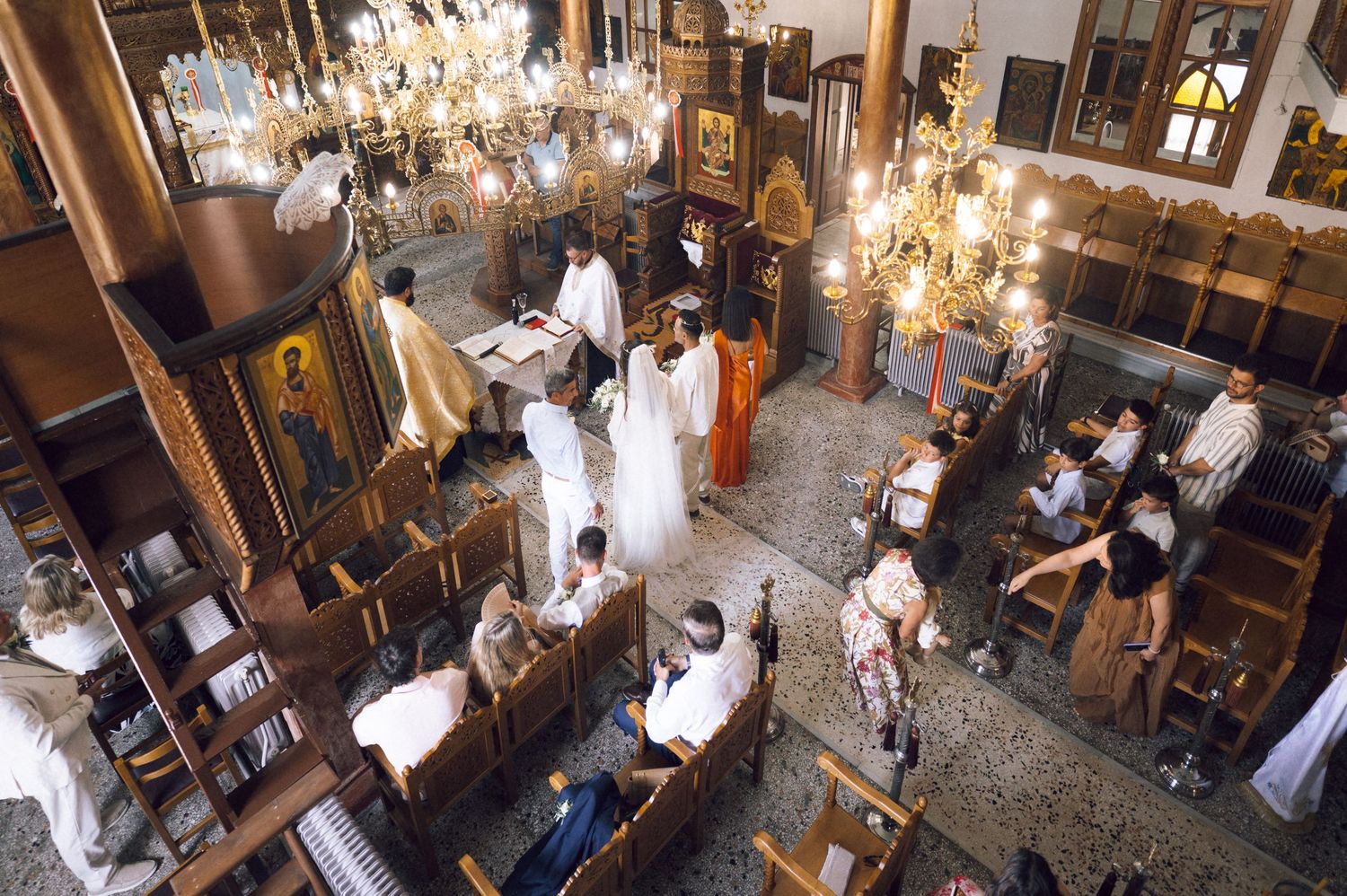 Orthodox church interior with worshippers during a religious ceremony, featuring ornate chandeliers and golden icons.