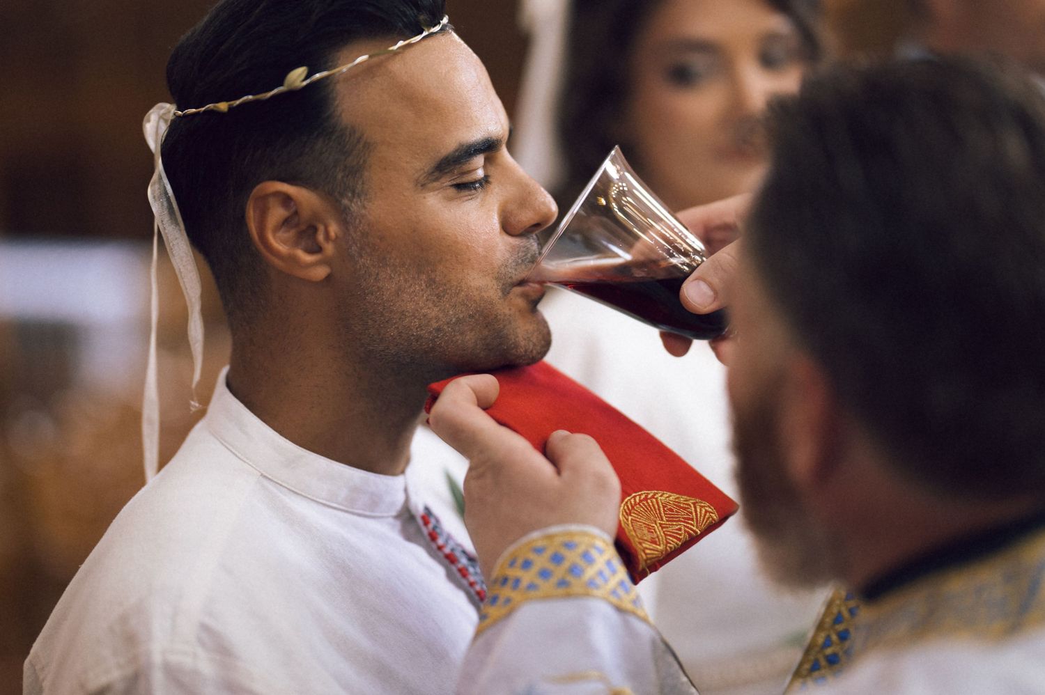 Man in white ceremonial attire drinking from a chalice during a religious communion ceremony.