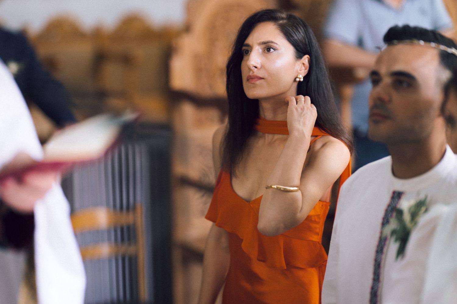 Woman in orange dress attentively listening at a religious ceremony inside a church.