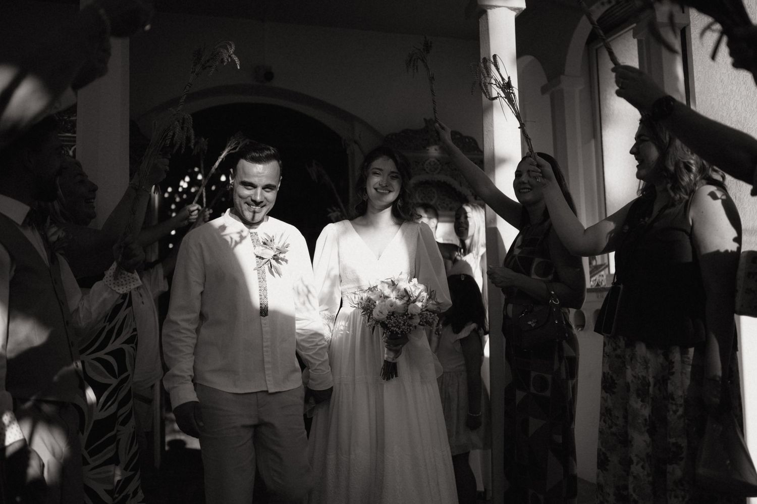Black and white photo of a smiling newlywed couple exiting a ceremony as guests celebrate around them.