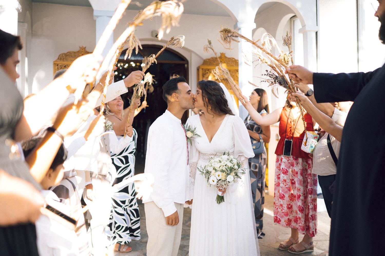 Bride and groom kissing under sparklers during outdoor wedding ceremony exit with guests celebrating.