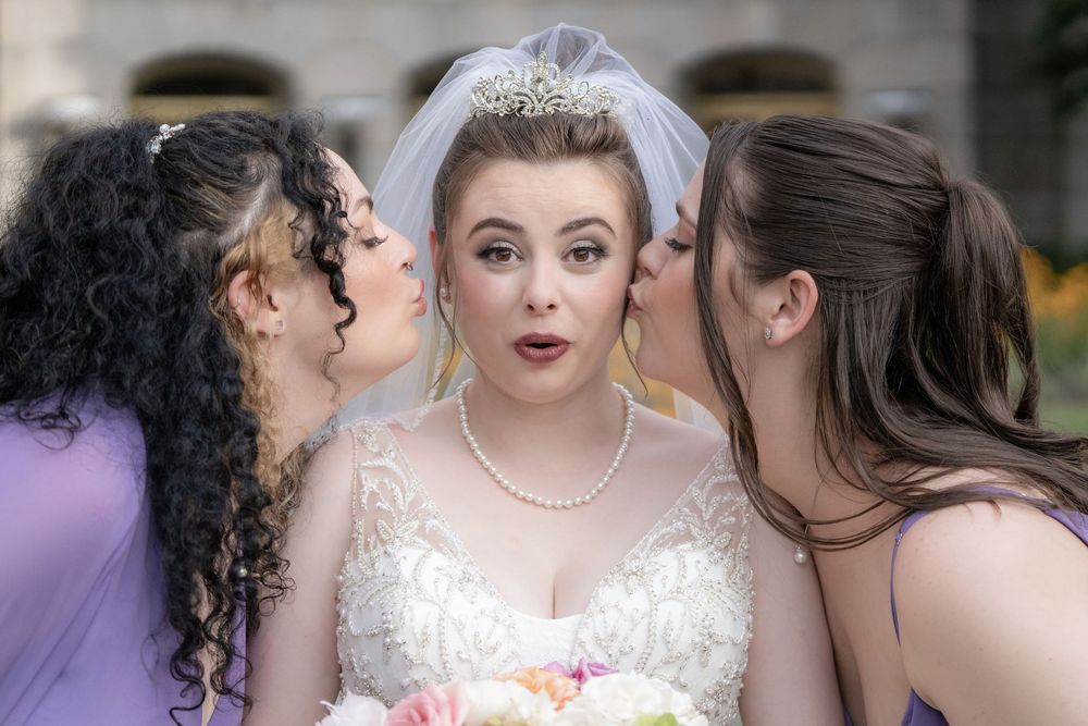 Bride making a surprised face as two bridesmaids kiss her cheeks at The Galliard Center in Charleston, SC