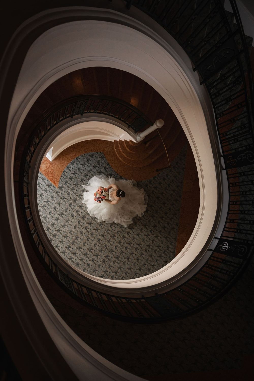 Bride standing at the base of a spiral staircase photographed from above at The Galliard Center in Charleston, SC