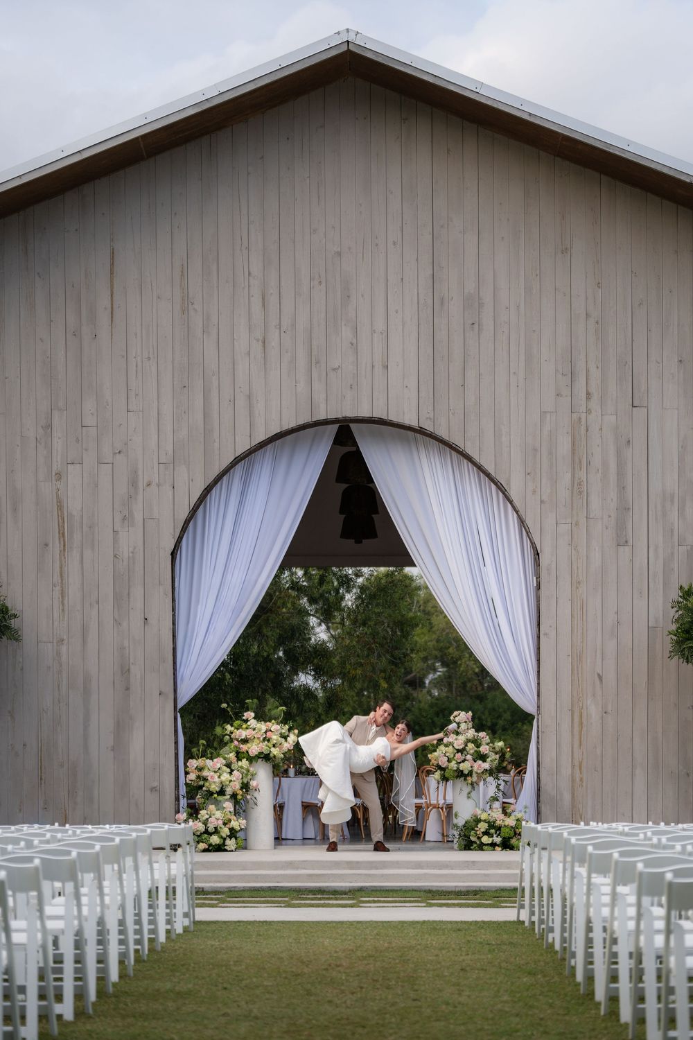 Groom carrying bride through open barn doors at White Trail Club in Jupiter, FL