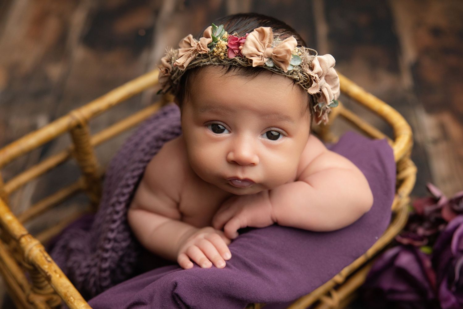 Sleeping newborn baby wrapped in teal swaddle inside a small bucket with a green pillow.