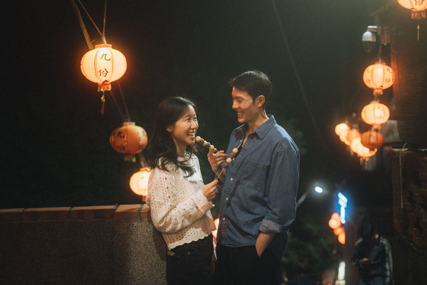 Couple sharing a romantic moment under glowing Chinese lanterns at night in an outdoor setting.