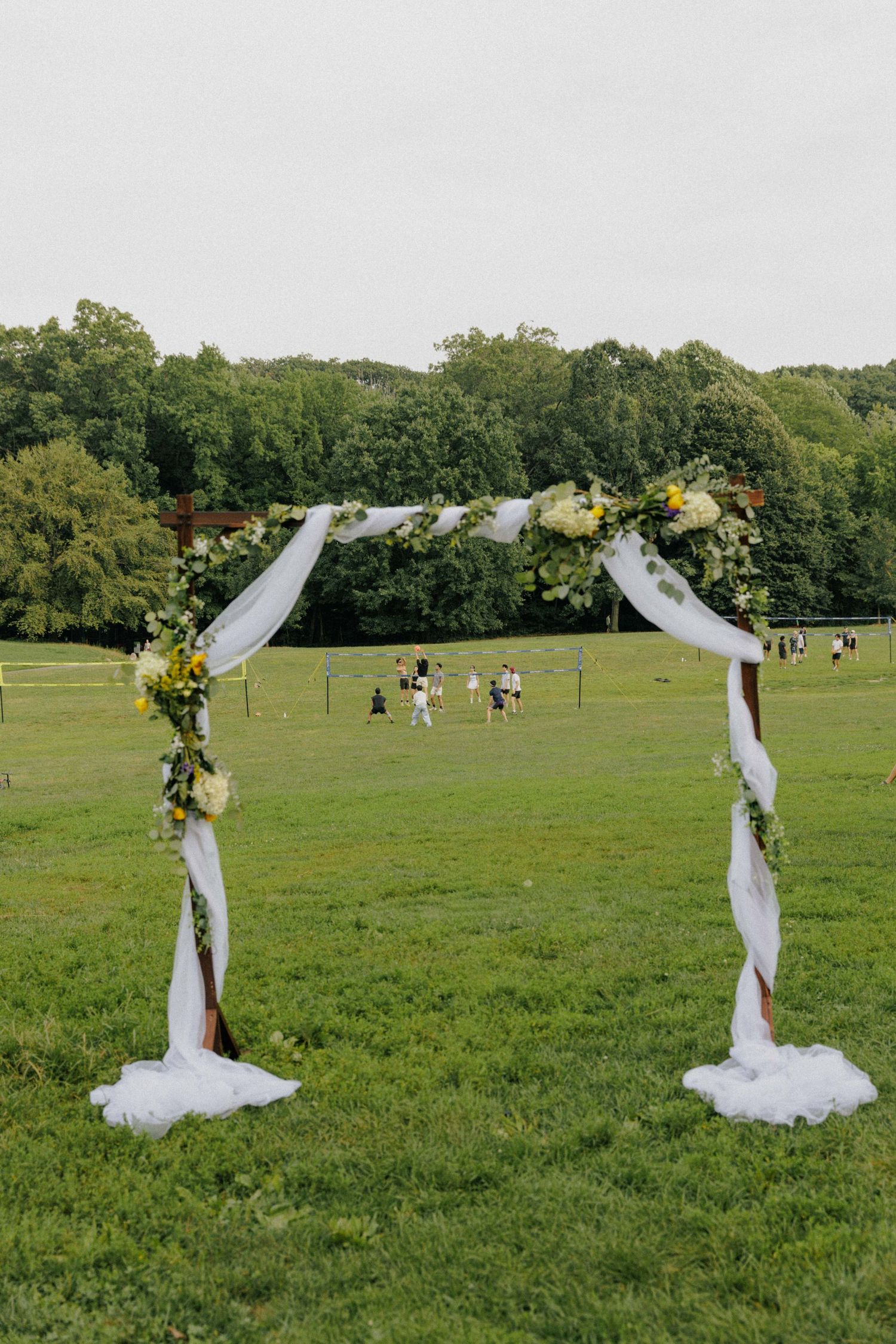 Elegant outdoor wedding arch adorned with white fabric draping and yellow floral arrangements on a lush green lawn.