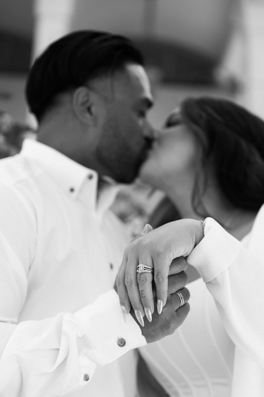 Black and white photo of a couple kissing while the woman displays a sparkling diamond engagement ring on her hand.