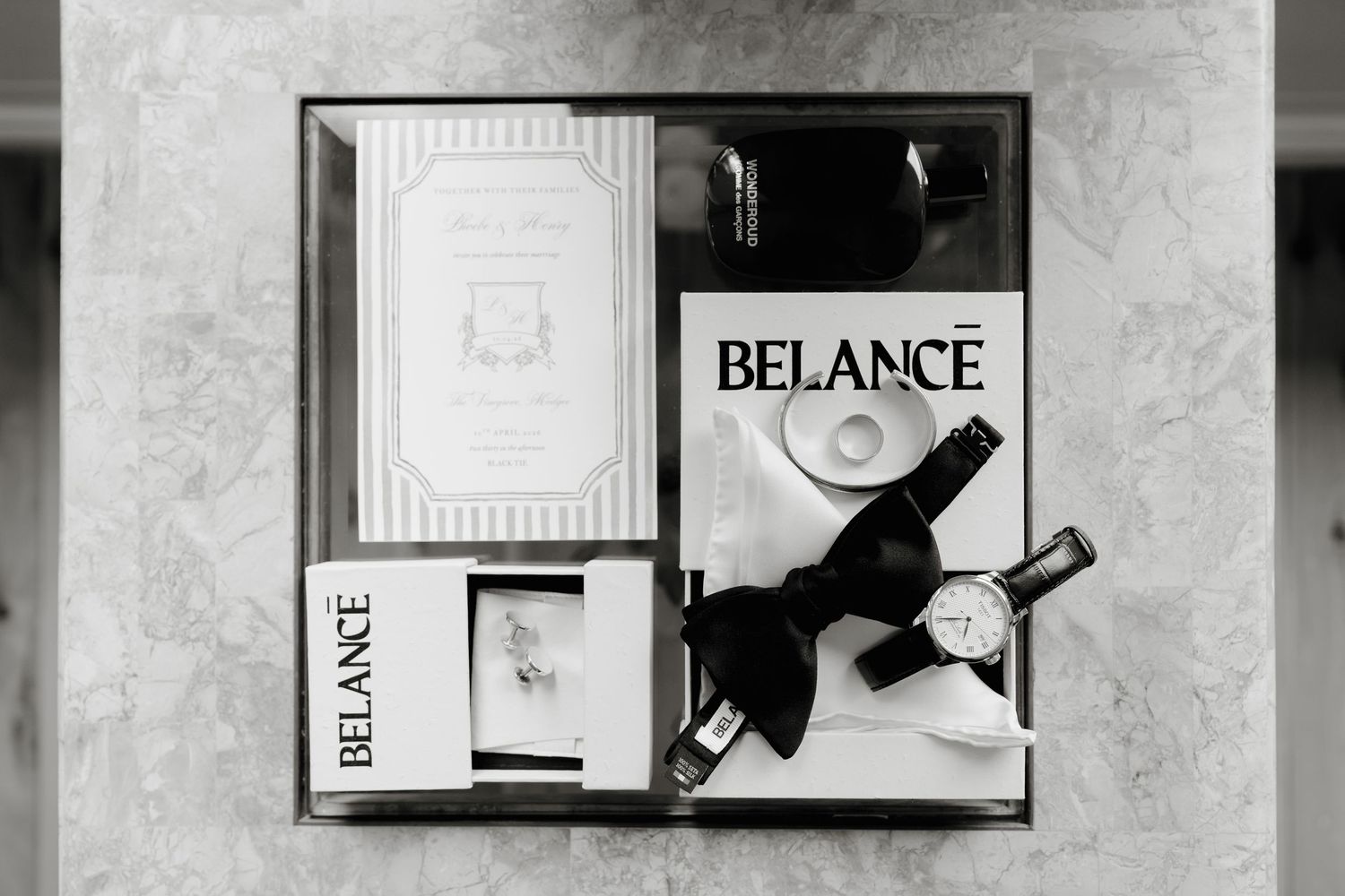 Black and white flat lay of Belance wedding stationery, bow tie, watch, and ring on marble surface. The Vinegrove Mudgee. Mudgee Wedding