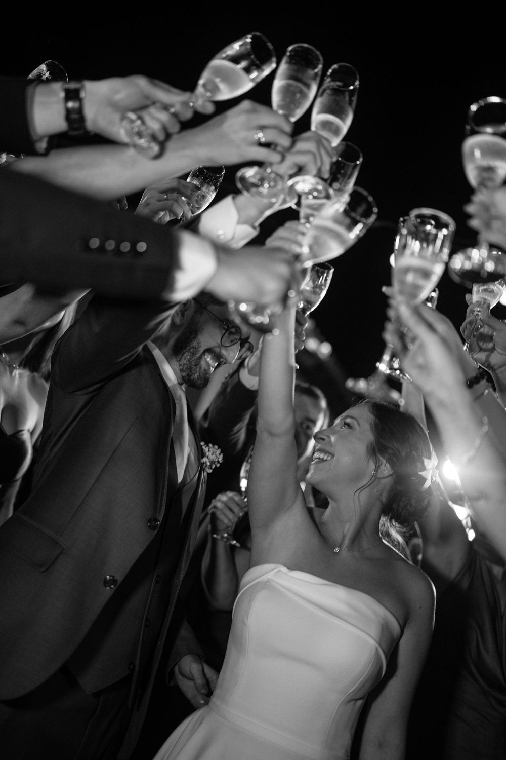Wedding guests raising champagne glasses in a joyful toast with the bride in black and white.