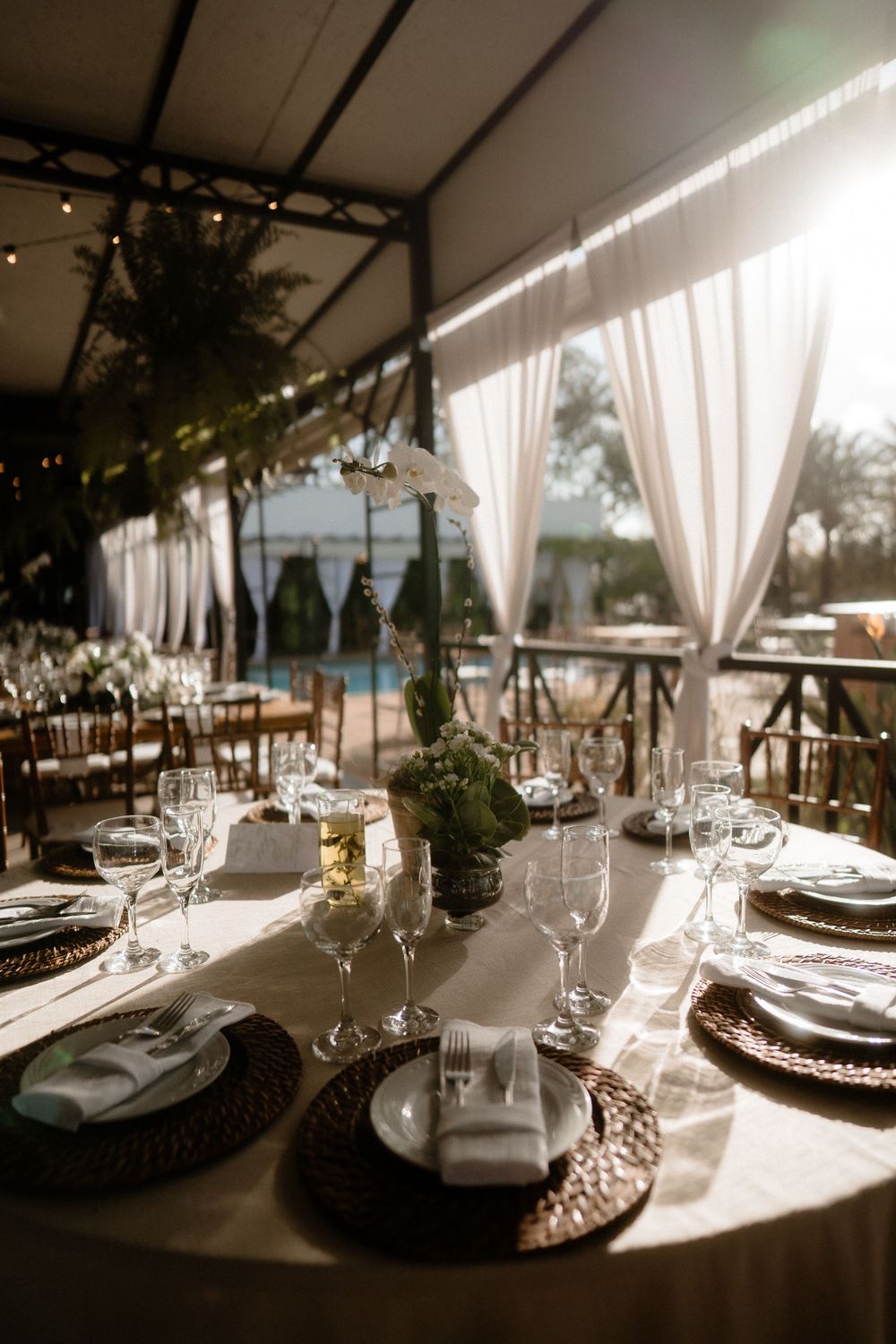 Elegant outdoor wedding reception table setting with white drapes and glassware.