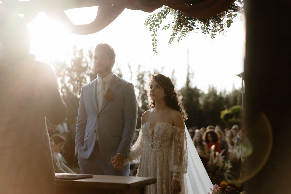 Bride and groom hold hands at the altar bathed in warm golden sunlight during ceremony.