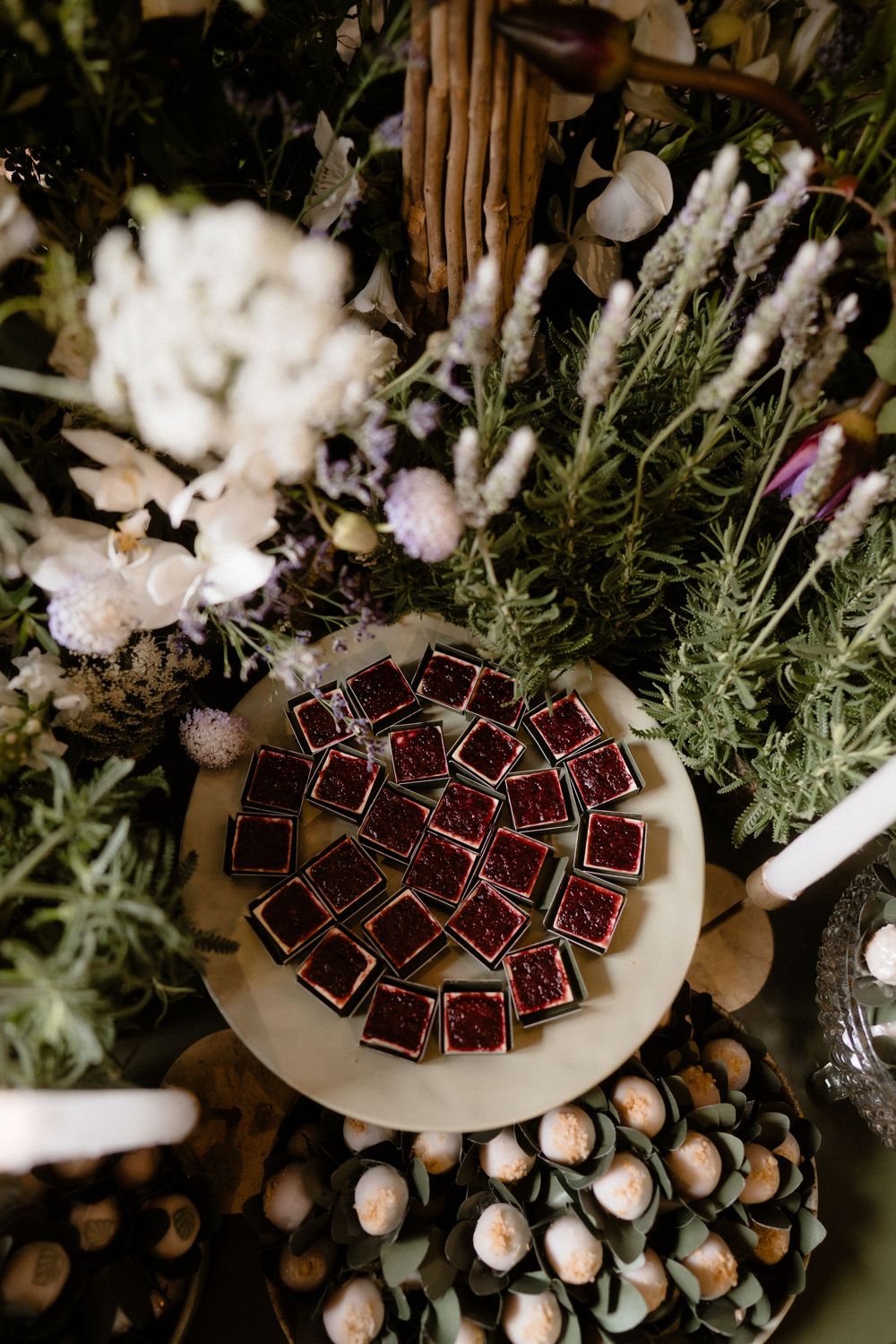Aerial view of ruby red chocolate desserts arranged on a wooden cake stand surrounded by lush greenery and dried flowers.