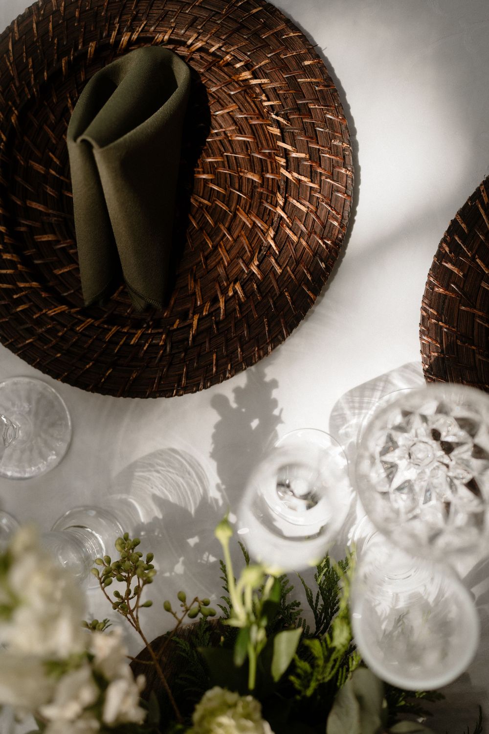 Elegant wedding table setting with woven charger plates, crystal glassware, and white floral centerpiece arrangement.