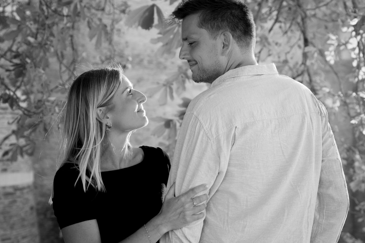 Couple en noir et blanc, regards complices sous un feuillage, séance photo de couple à Lyon