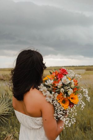 Woman with dark hair seen from behind holding a vibrant bouquet in an open field.
