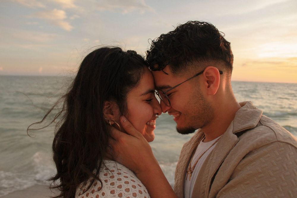 A romantic couple touching foreheads tenderly on a beach during a stunning sunset.