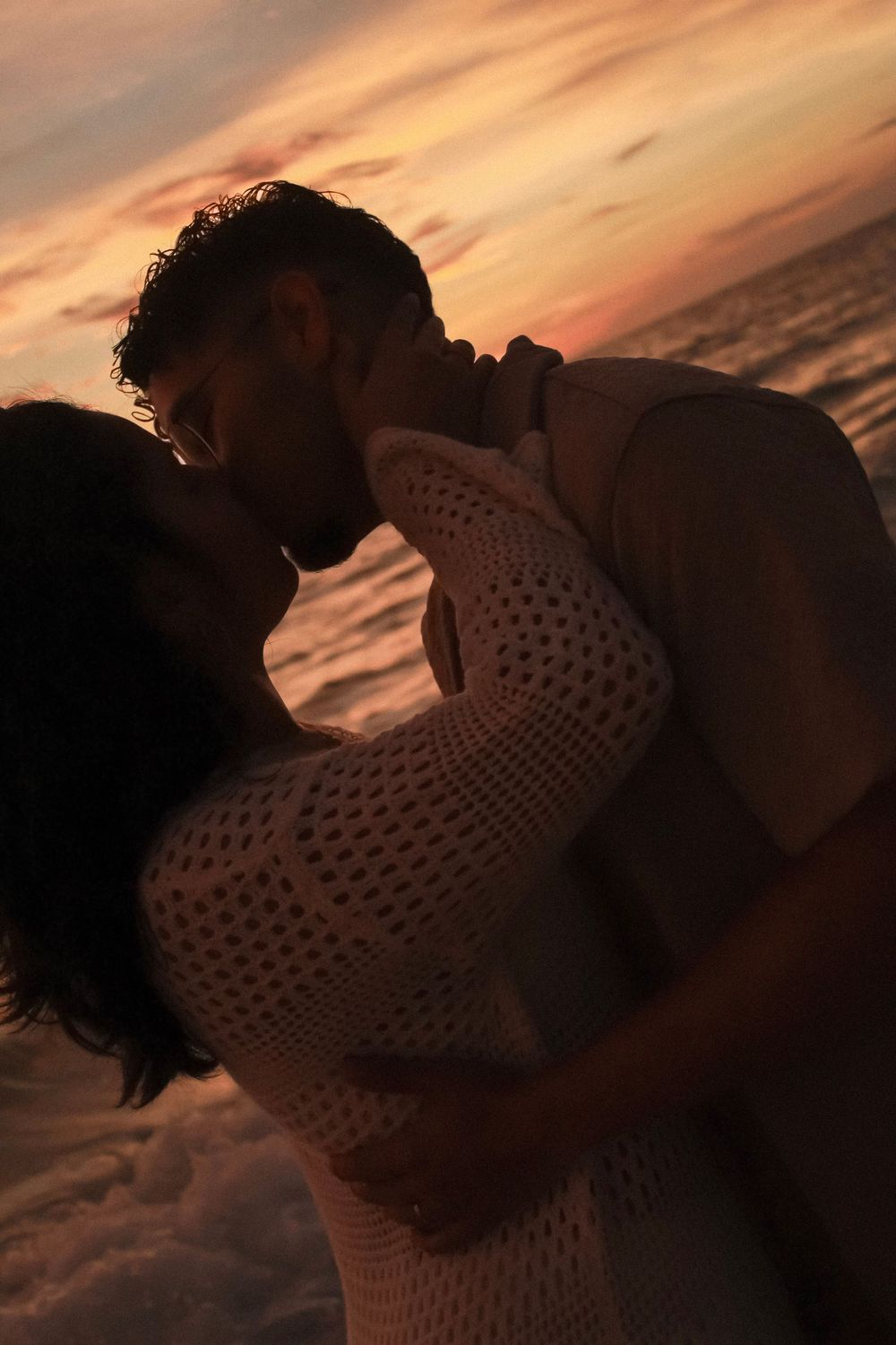 A couple sharing a passionate kiss silhouetted against a dramatic colorful ocean sunset.