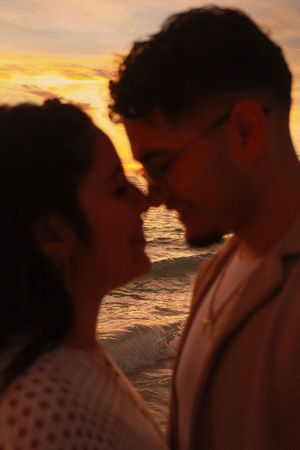 Silhouette of a couple almost kissing at golden hour with ocean waves glowing behind them.