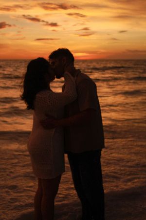 Silhouette of a couple kissing on the beach against a dramatic orange and red sunset sky.