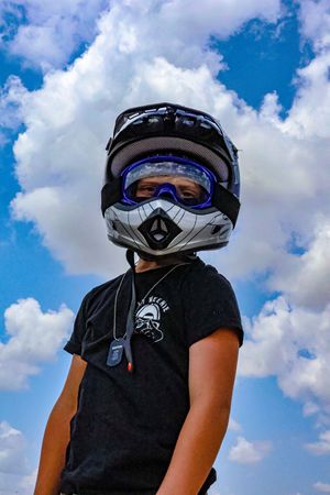Creative portrait of a motocross rider wearing a helmet against a bright blue summer sky.