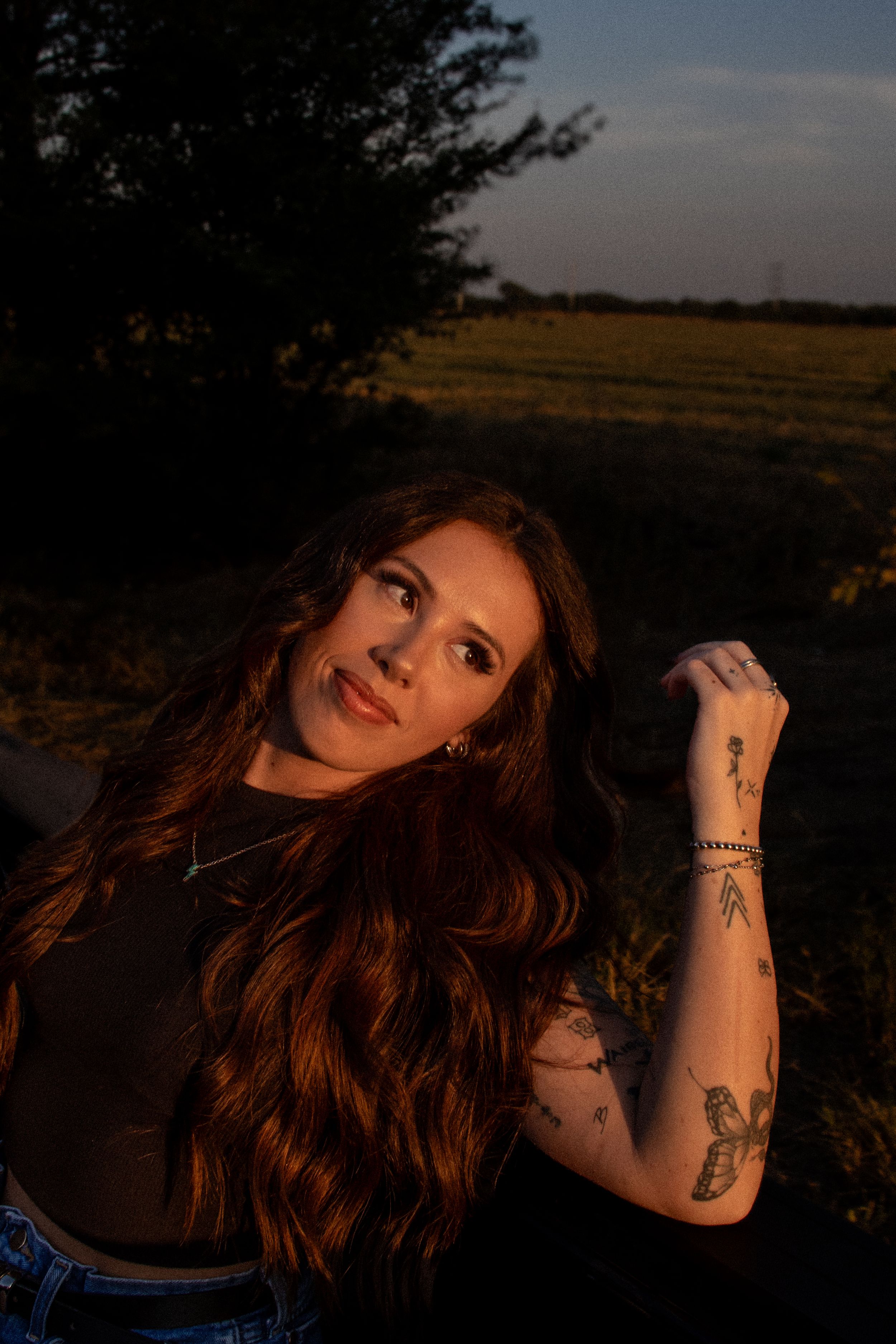 Woman with long red hair posing outdoors at sunset during a warm, cinematic portrait session.