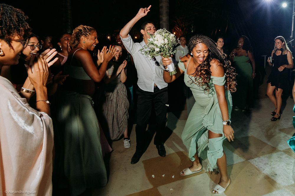 Guests dancing joyfully at a wedding reception, with a woman in green holding a bouquet on the dance floor.