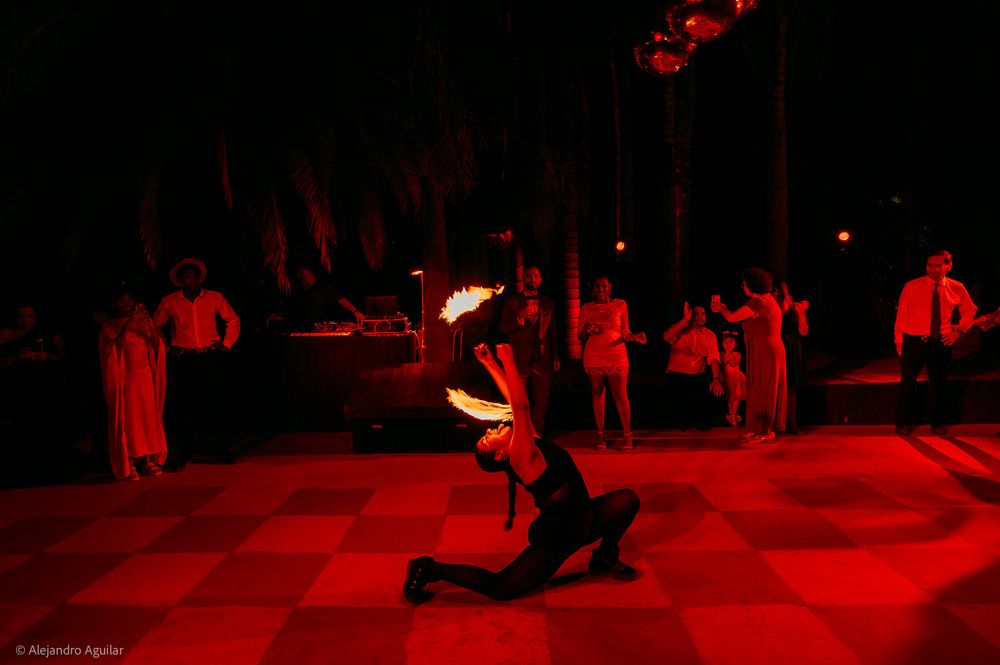 Fire dancer performing dramatic floor routine with spinning flames under red lights at an outdoor nighttime event.