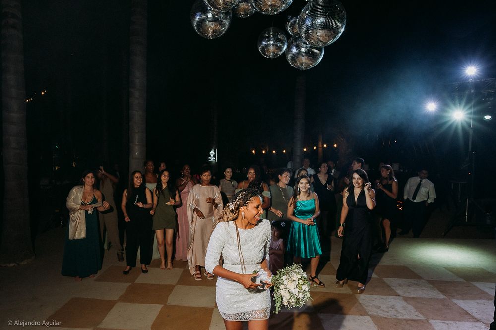 Bride in white dress tosses bouquet to guests at elegant outdoor wedding reception with disco ball lighting.