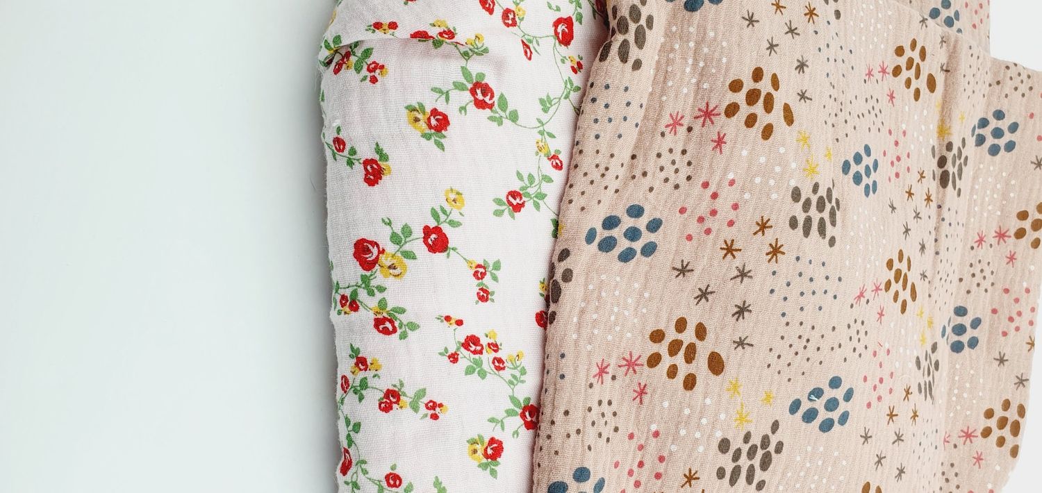 Two rolled fabric bolts with floral and dotted patterns in soft pink and white tones displayed against a white background.