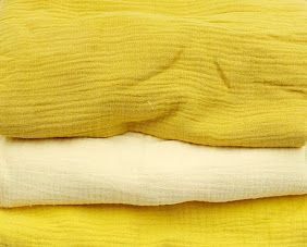 Stack of folded yellow and white muslin cotton fabric swaddle blankets in bright lemon and cream tones.