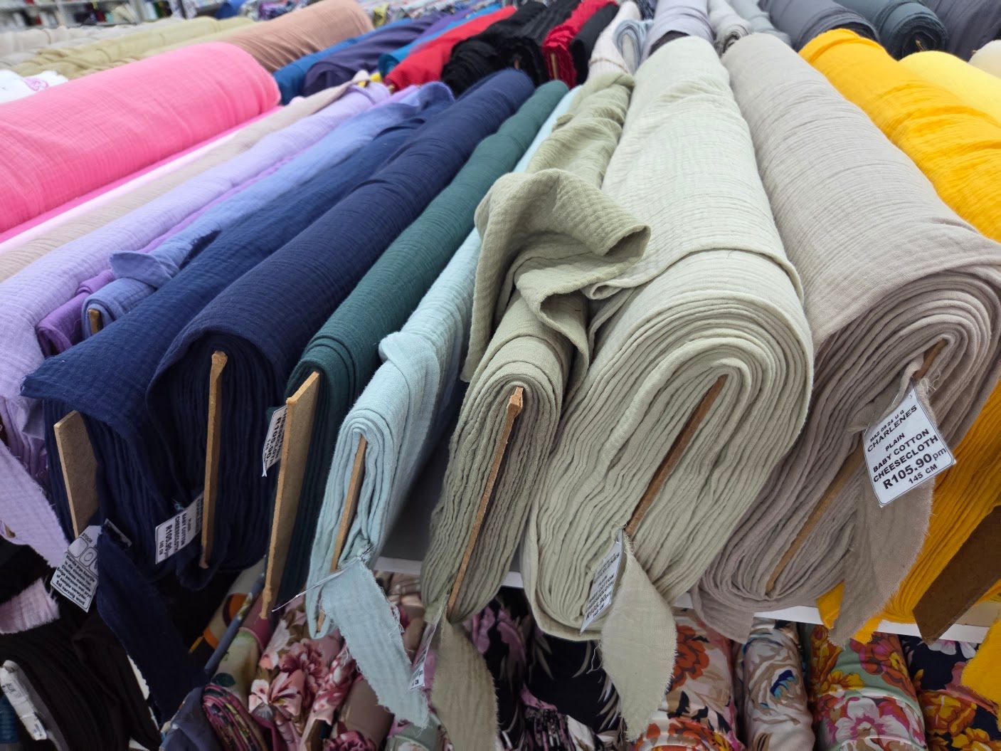 Colorful rolls of fabric neatly stacked on display at a textile market, featuring various colors including pink, blue, and beige.