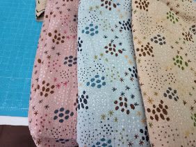 Four folded fabric pieces with floral and star patterns in pink, blue, and beige tones displayed on a cutting mat.