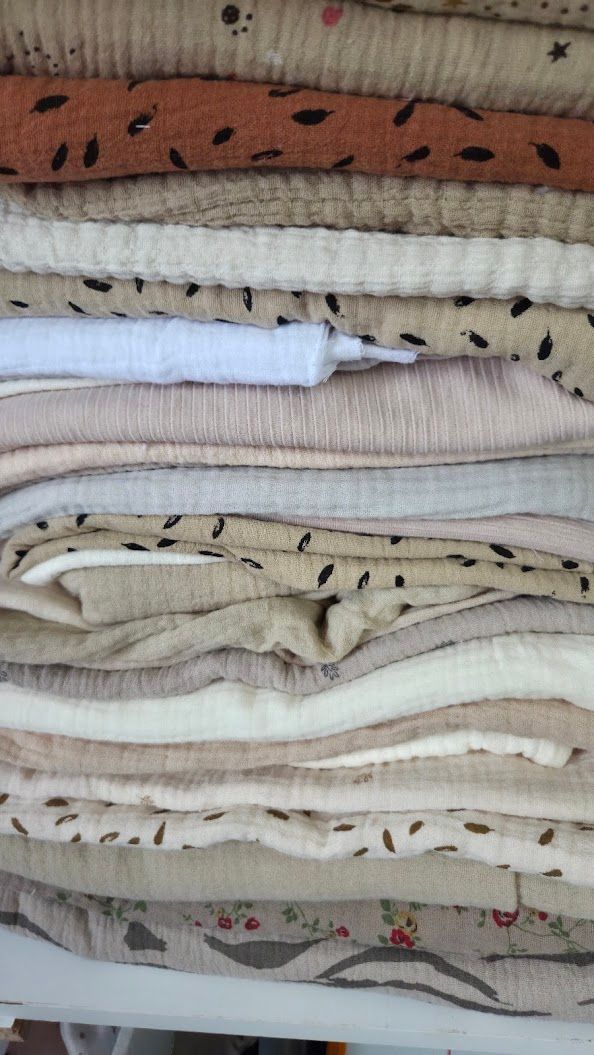 Stack of neatly folded muslin fabric in neutral tones with leaf prints, including beige, blush pink, and white layers.