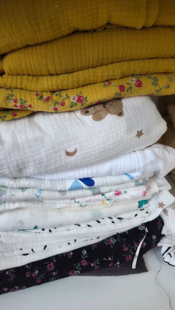 Stack of folded baby muslin swaddle blankets in mustard yellow, floral, and bear print patterns.