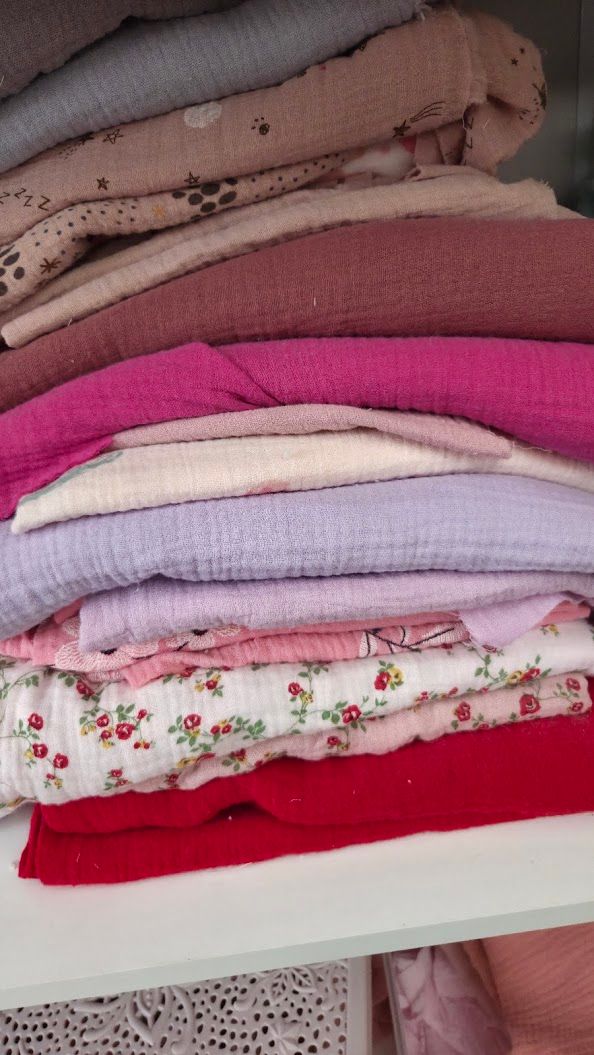 Neatly folded stack of pink, red, purple, and floral fabric pieces arranged on a white shelf.