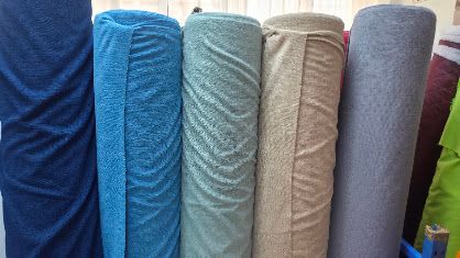 Five rolled fabric bolts in navy, teal, sage, beige, and tan textured materials displayed upright side by side.