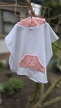White hooded baby poncho with pink floral trim and pocket, hanging on a branch outdoors.